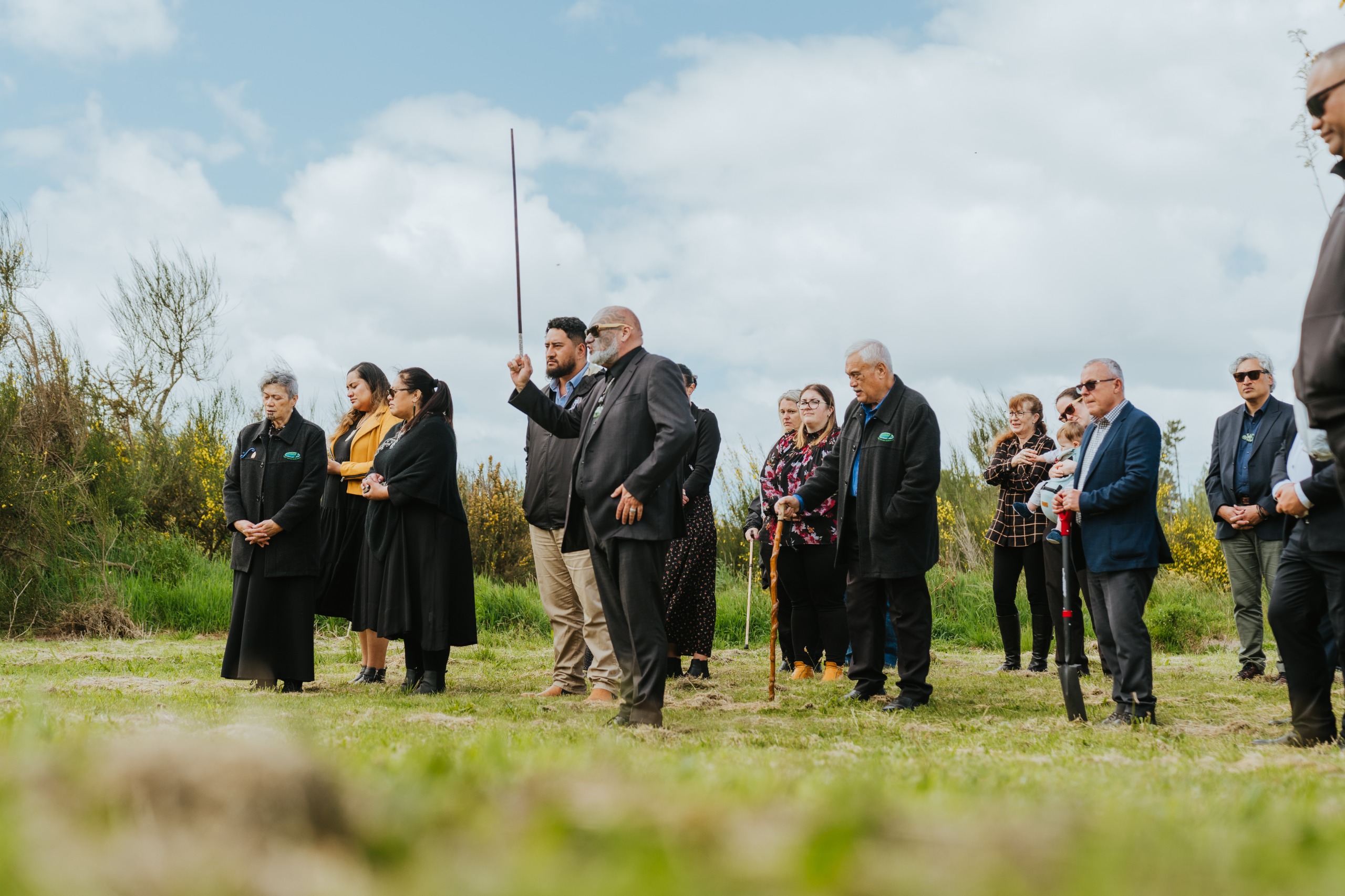 people gathered outside with shovels ready to plant two kowhai trees